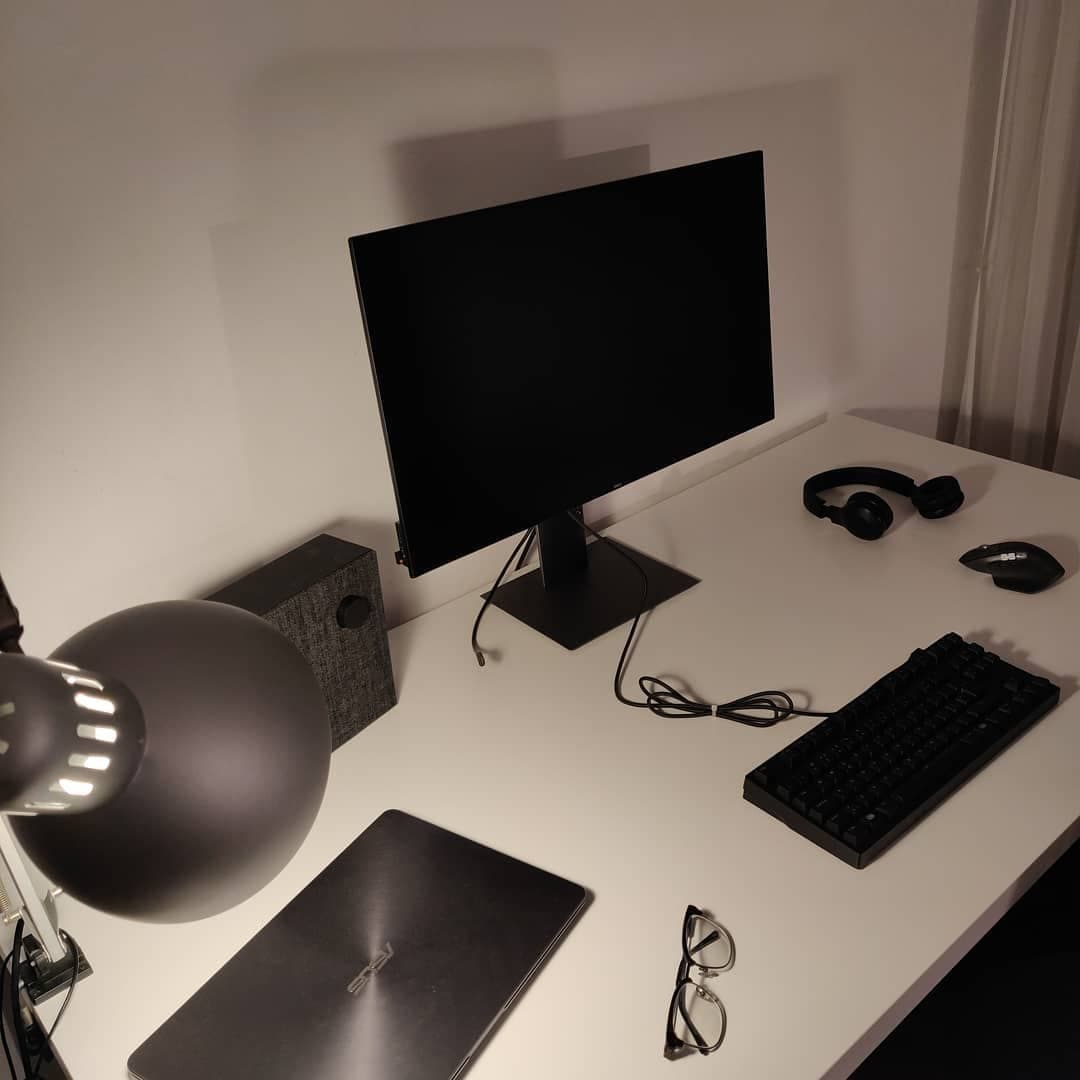A minimal white desk with a monitor, keyboard and headphones