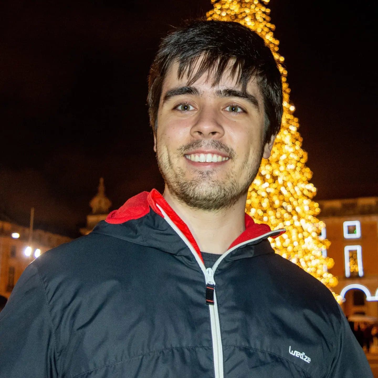 Rodrigo smiling at night by the Christmas tree in Praça do Comércio, Lisbon
